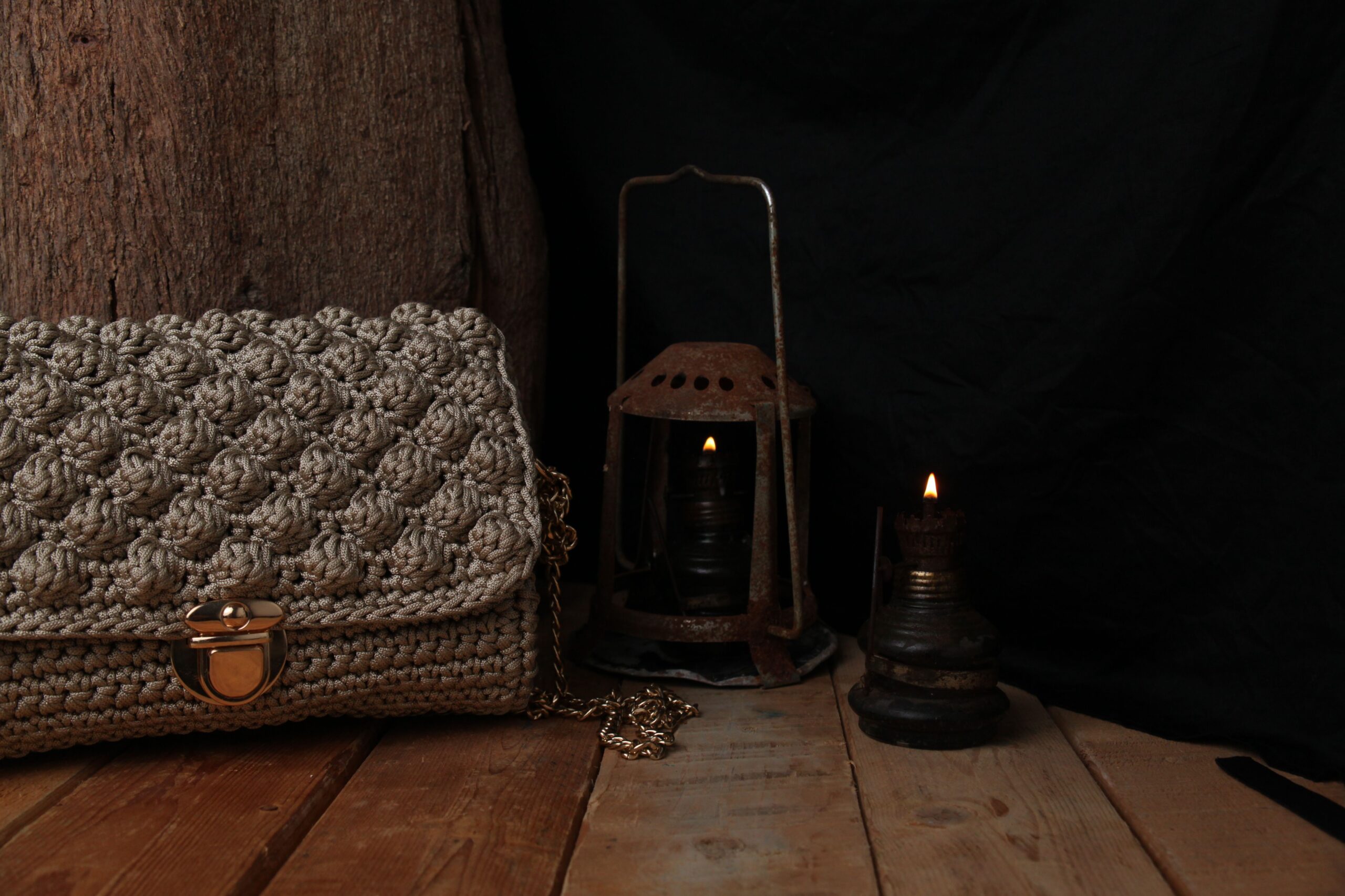Warm rustic scene featuring a knitted bag and ambient lantern lighting on wooden table.